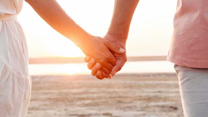 A close-up of a couple holding hands on the beach