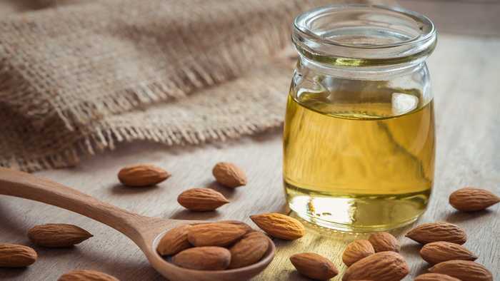 Almond oil in a jar with a ladle full of fresh almonds