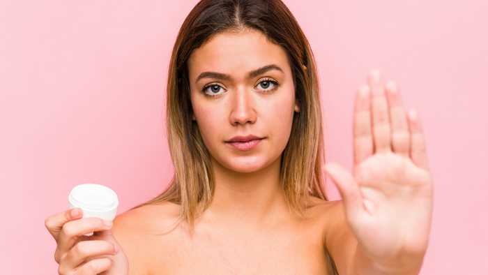 Woman holding a moisturiser with outstretched arm as to say stop