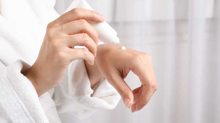 Lady moisturising her hands in a bath robe