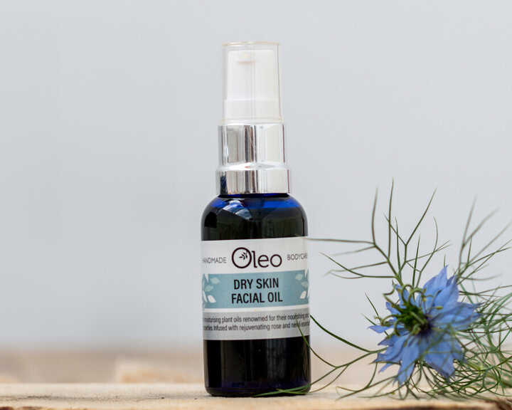 Bottle of dry skin facial oil on a wooden surface with a blue flower beside it.