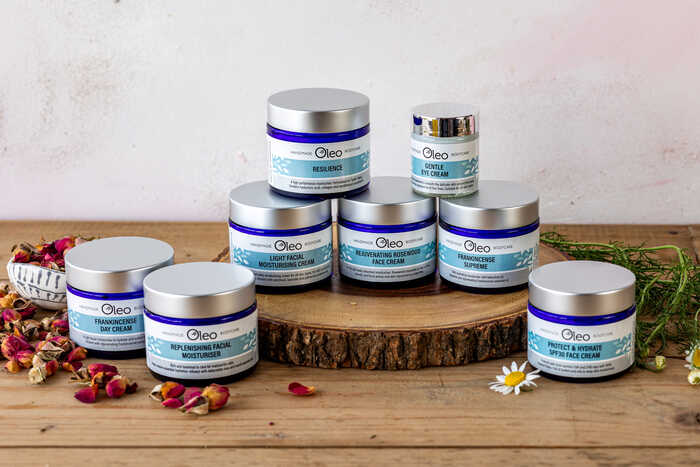 Assorted skincare products from Oleo arranged on a wooden surface with flowers and herbs.