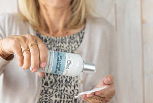 A woman pours liquid from a bottle onto a cotton pad.