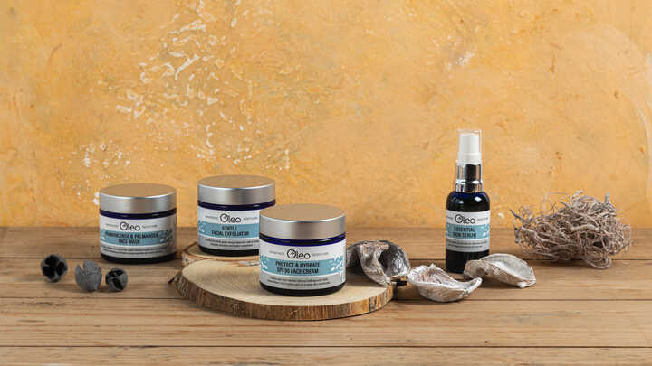 Oleo skincare products and seashells on a wooden surface against an orange background.