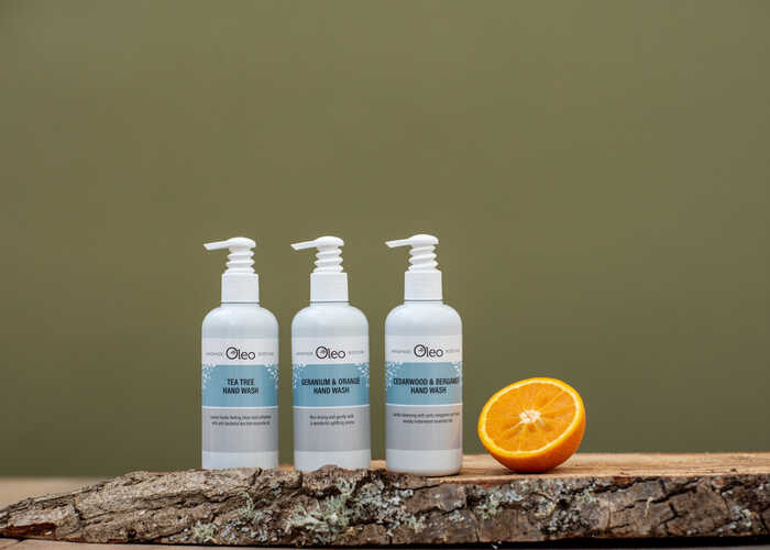 Oleo Bodycare vegan hand wash placed on a wooden log slab with half an orange to showcase the natural ingredients used