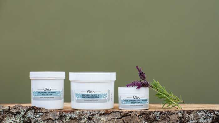Essential oil based massage balms by Oleo Bodycare place upon a wooden stump with a sprig of fresh lavender