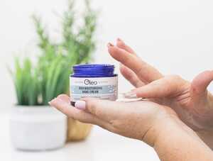 A hand holding a Oleo hand cream against a background of greenery.