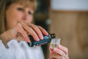 A woman pours liquid from a dropper bottle into a small measuring cup.