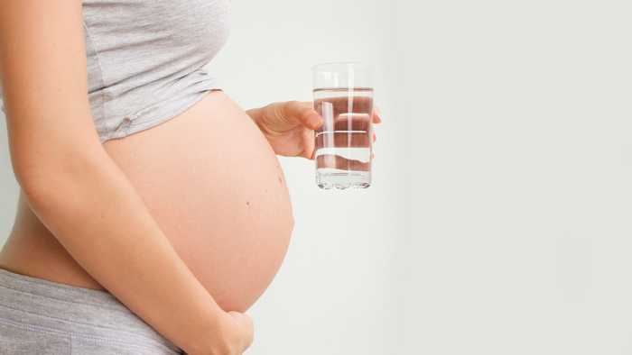 Pregnant lady holding a glass of water to keep up hydration during pregnancy